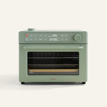 A sage green countertop oven with digital display showing 425°F and 24:59, a control knob, buttons, and a glass door revealing cooking racks inside.