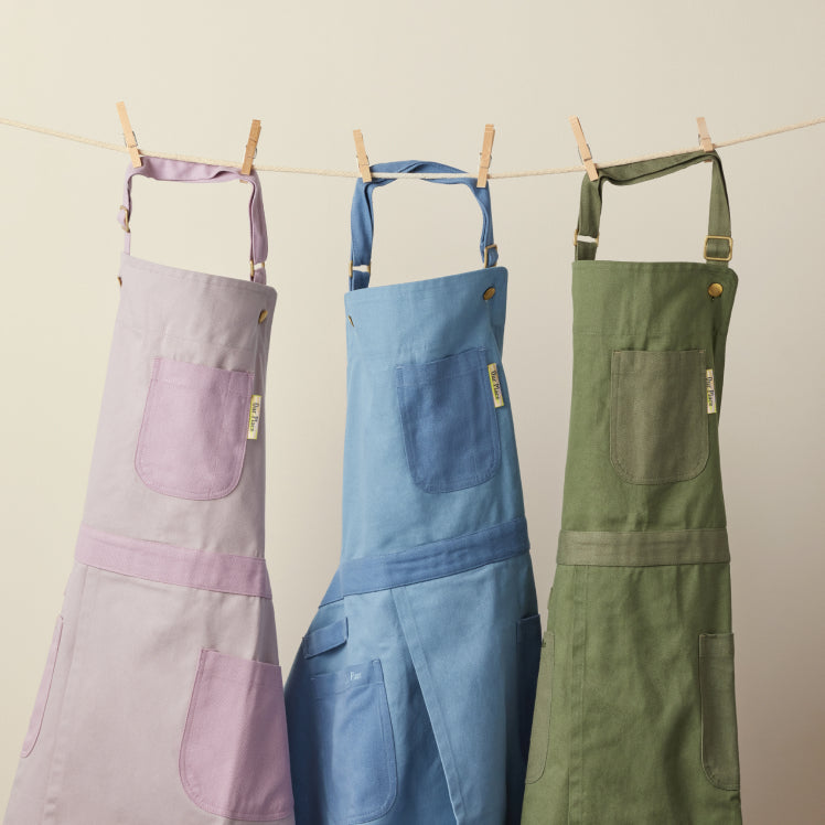 A purple, blue, and green Home Cook Apron hang from a clothesline