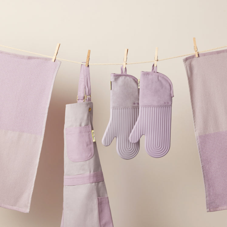 Purple Home Cook Apron, Hot Mitts, and Double Dish Towels hanging from a clothesline