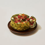 A round spinach and cheese frittata topped with cherry tomatoes sits on a brown plate, with one wedge cut and slightly separated.
