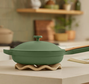 Green frying pan with wooden handle on a wavy stand in a kitchen setting