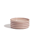 A stack of four light pink ceramic plates on a white background with a faint shadow to the left.
