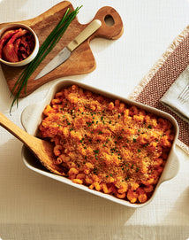 Baked mac and cheese dish in a white casserole dish with a wooden spoon on a light background.