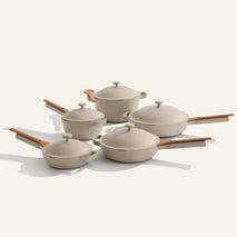 The Cookware Set+ includes five beige nonstick ceramic pieces with wooden handles and lids, beautifully arranged on a plain light background.