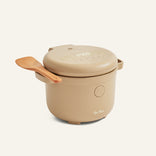 The Rice Cooker, in beige, features a digital display on the lid and comes with a wooden spoon resting on its handle, set against a plain background.