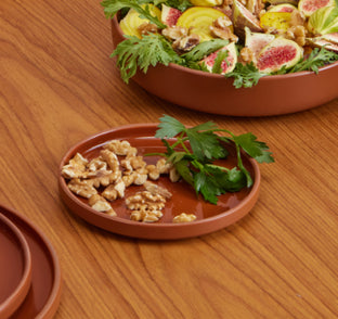 Terracotta clay salad plates on a wooden table, with one plate in the foreground holding walnuts and parsley and another plate in the background filled with figs, walnuts, and greens.