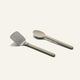 A stainless steel spatula and a tan serving spoon from a Titanium Pro Utensil Set lying side by side.