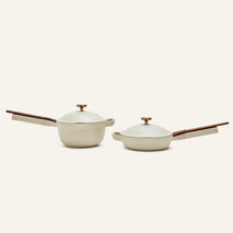 The Mini Cookware Duo—two beige multi-use pans with wooden handles and matching lids—is displayed on a plain light background.