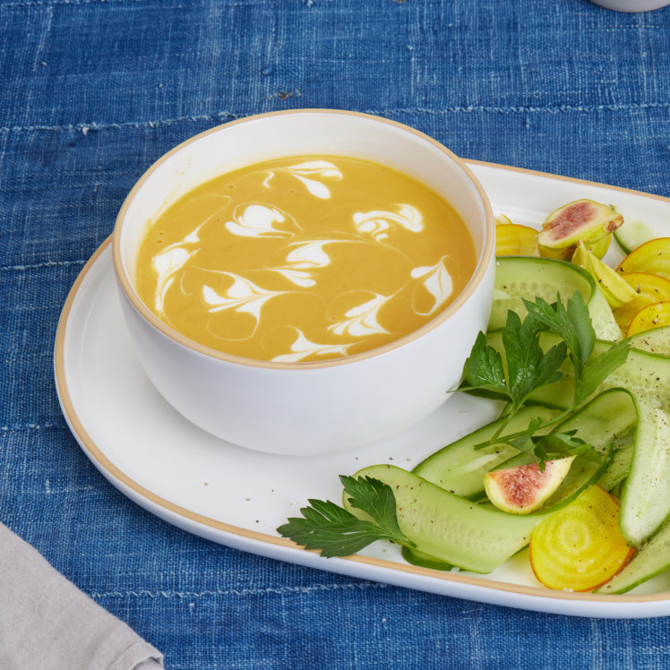 white soup bowl with soup set on white serving platter with vegetables