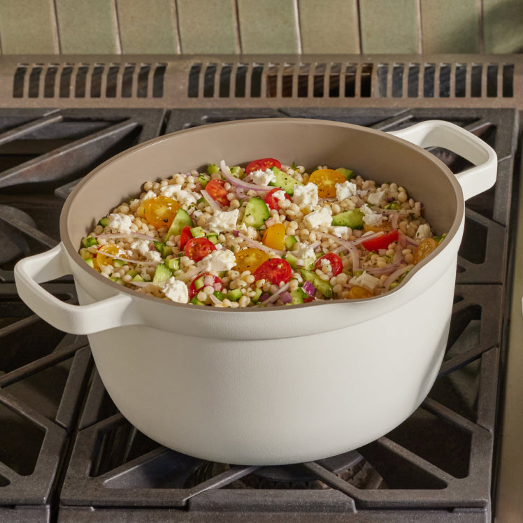 A vibrant coucous dish with tomatoes, cucumbers, and feta cooks in a white Perfect Pot on the stove